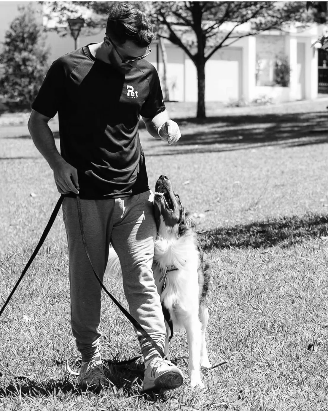 Jairo Sánchez de pie, dando una señal con la mano a un perro que lo mira desde abajo, atento, en blanco y negro.